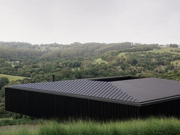 The black-pigmented concrete mass firmly anchors the structure to the ground while the black timber battens shelter the living spaces from the western sun