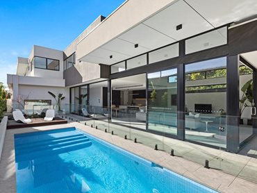 The massive IGU-equipped sliding doors visually connect the interior to the luxurious backyard pool area