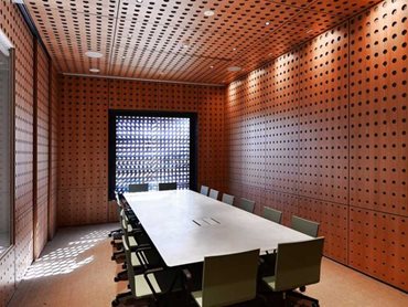 In the building’s office and conference rooms, perforated panels have been used on the walls and ceilings in a rich amber toned timber 
